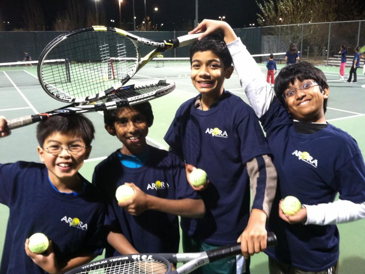 Young players in Arora Tennis shirts holding rackets and tennis balls