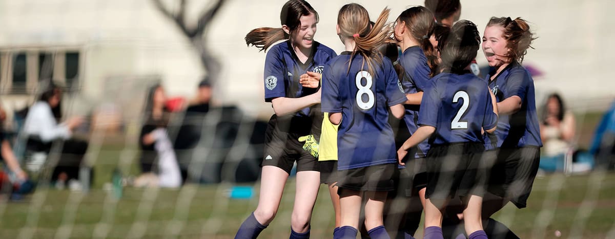 Girls in navy AYSO jerseys celebrating together on a grass field