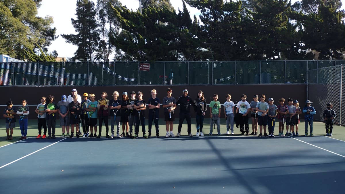 A line of young players holding rackets on a tennis court
