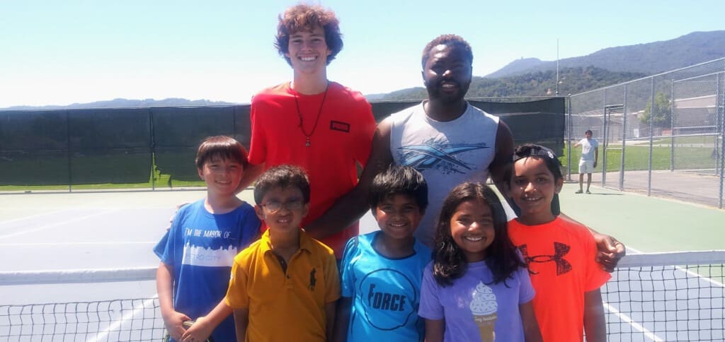 Young players posing with two coaches on a tennis court