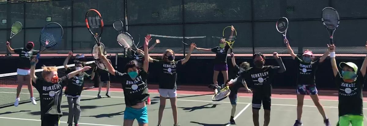A row of young players in club shirts raising their rackets on a court