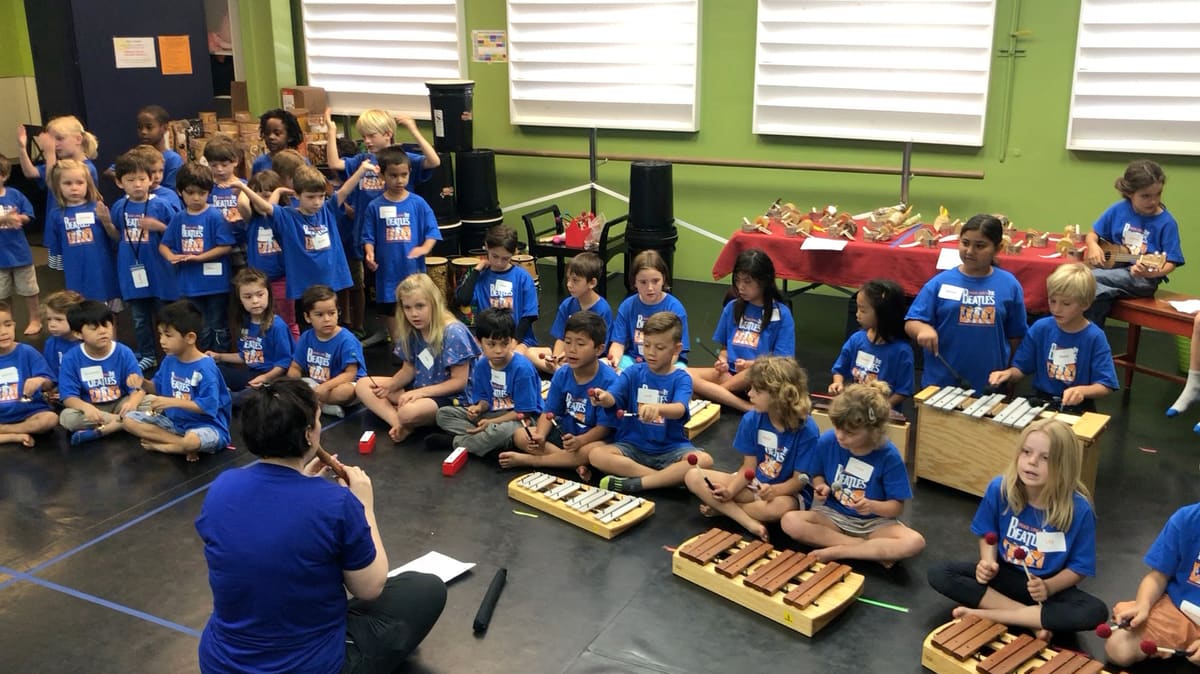 Children sitting on the floor playing xylophones and drums with a teacher at Bloom School