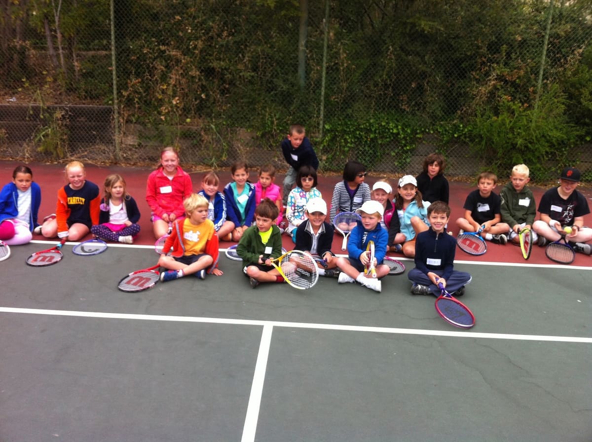 A big group of kids sitting with racquets on the Boyle Park tennis court