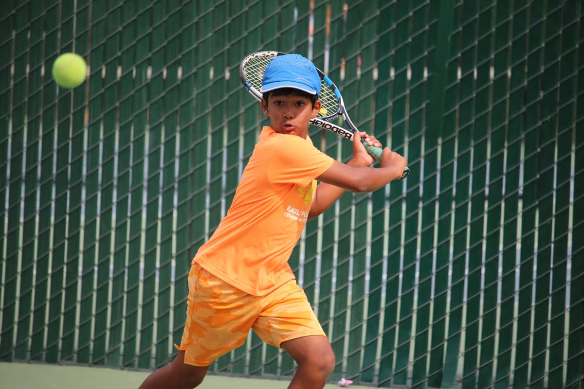 A young player in an orange shirt prepares a backhand