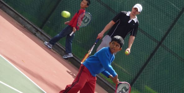 A coach and two young players on a tennis court