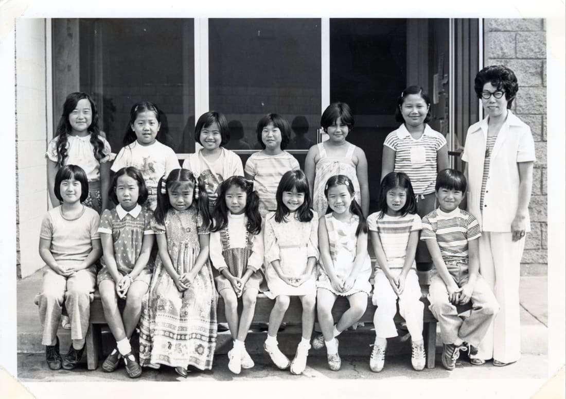 An old black-and-white class photo of language school students sitting with their teacher