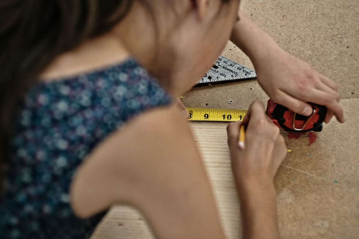 A girl measuring a piece of wood with a tape measure and pencil