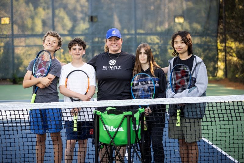 Young players and their coach holding rackets at the net