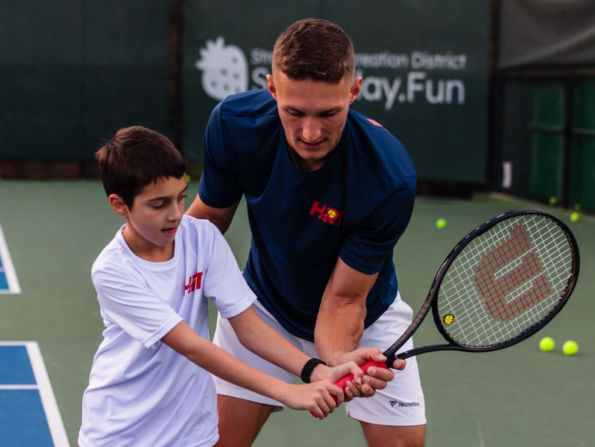 A coach helping a young player with his grip on a tennis racquet