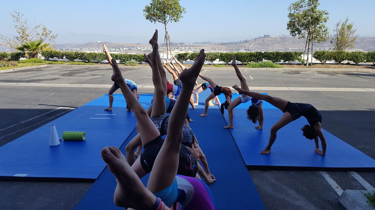 Young gymnasts doing bridges and leg lifts on blue mats outdoors