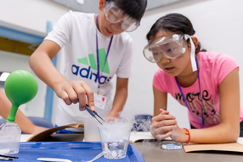 Two campers in safety goggles doing a chemistry activity with dry ice