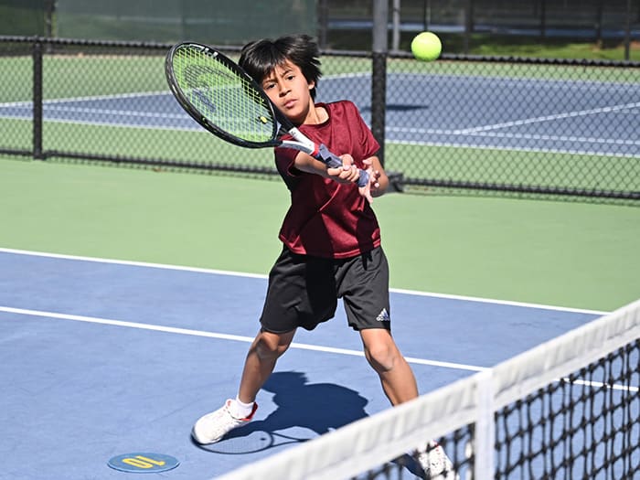 A boy hits a forehand on a blue and green court