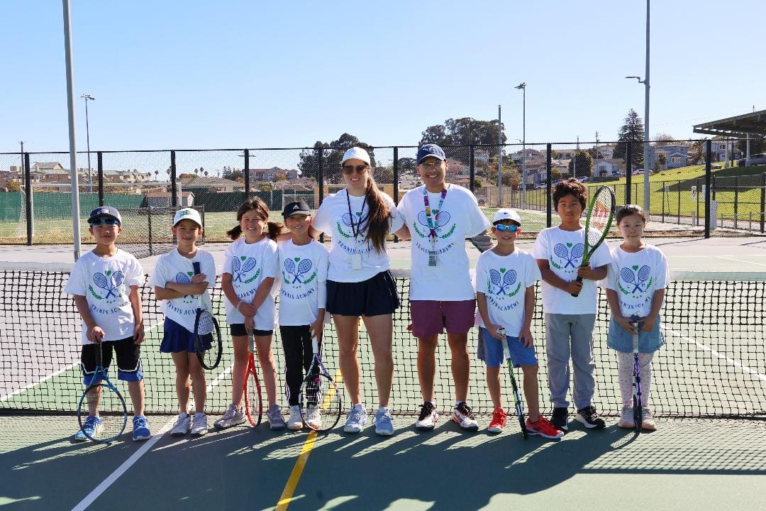 Two coaches and eight kids in matching shirts holding rackets at the net
