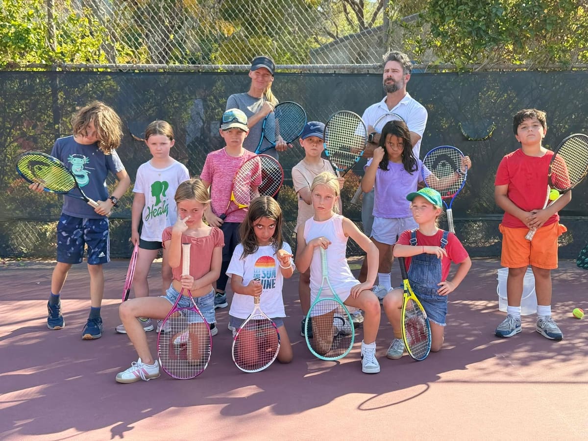 Kids and coaches holding racquets on a tennis court