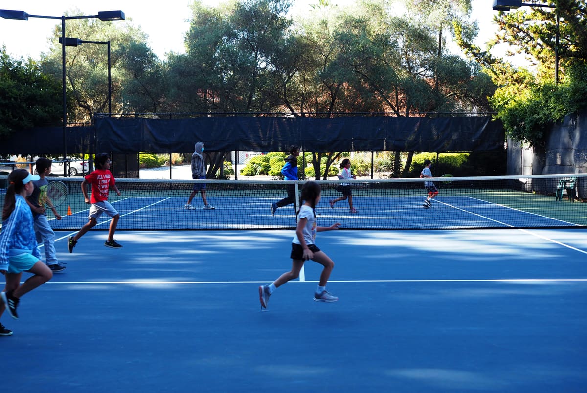 Kids running through drills on a blue tennis court