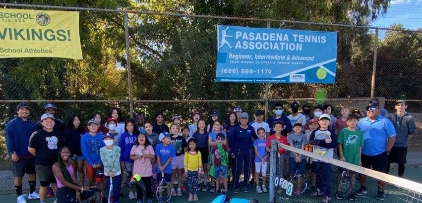A big group of kids with rackets and coaches on a tennis court