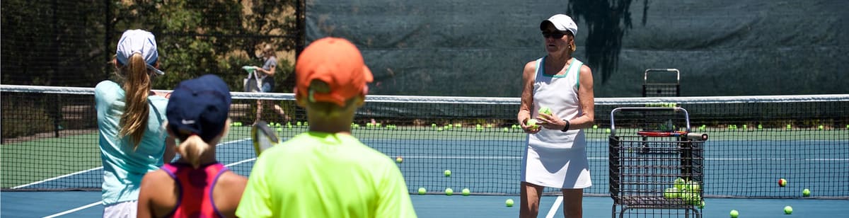 A coach feeding balls to kids on a tennis court