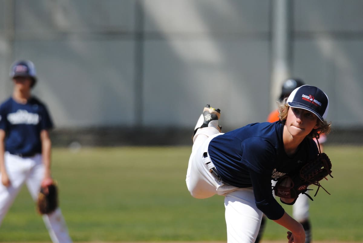 A young pitcher in a Santa Monica cap follows through on a pitch