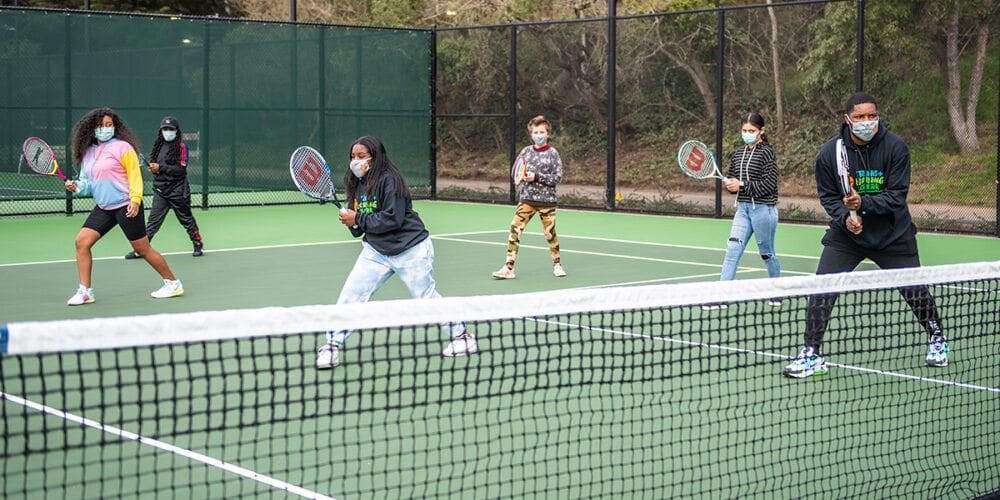 Students with racquets ready at the net during a tennis lesson