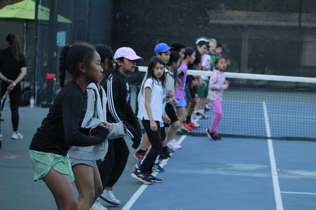 Kids lined up at the net warming up in a group class