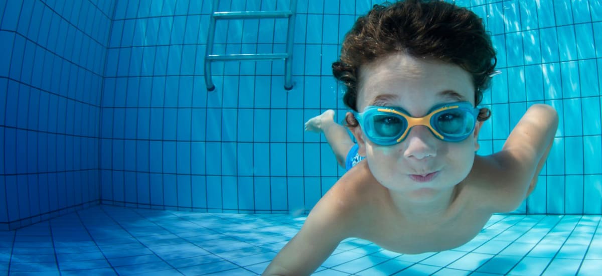 A boy in goggles swimming underwater in a pool