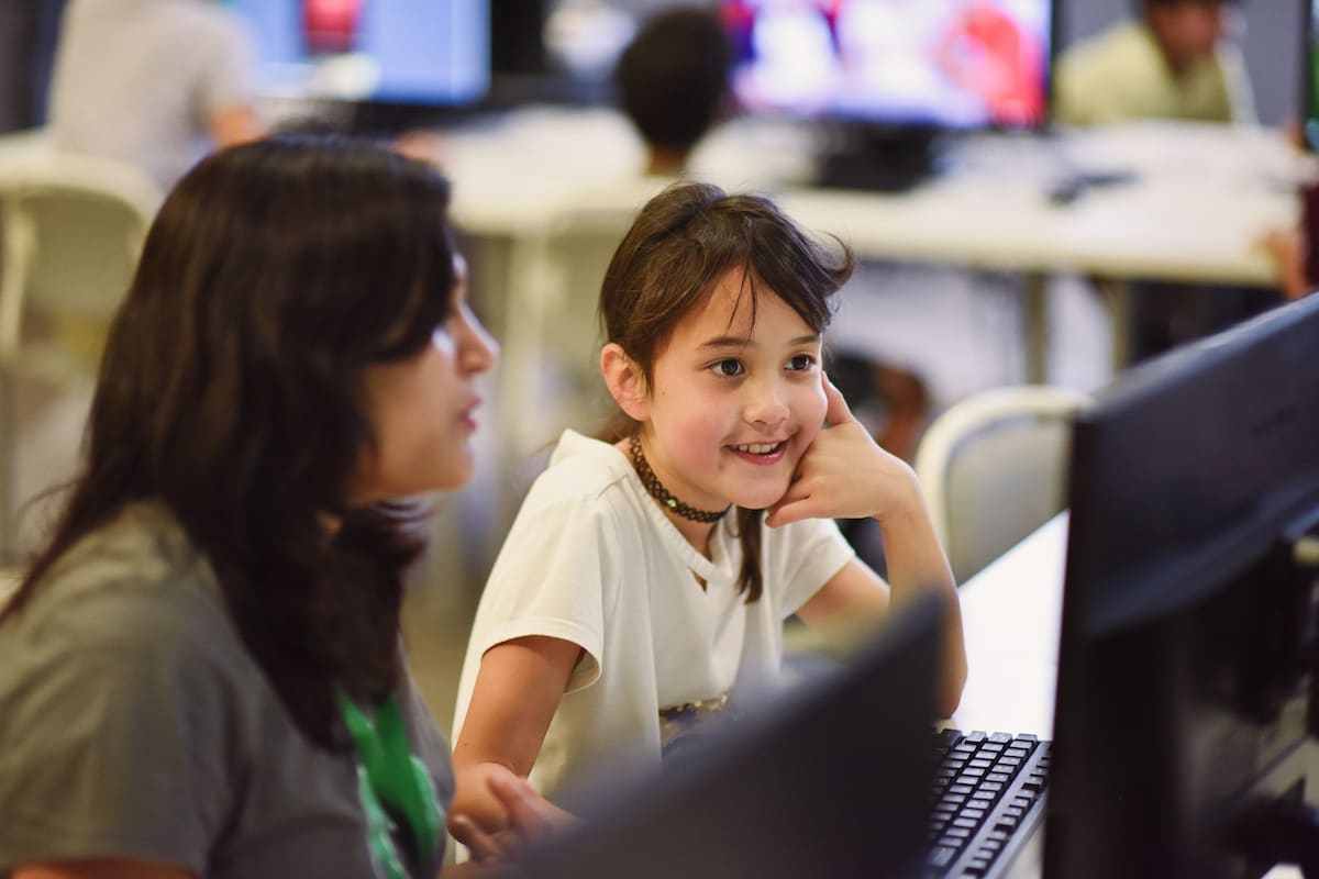 A girl smiling at her computer next to her coding coach
