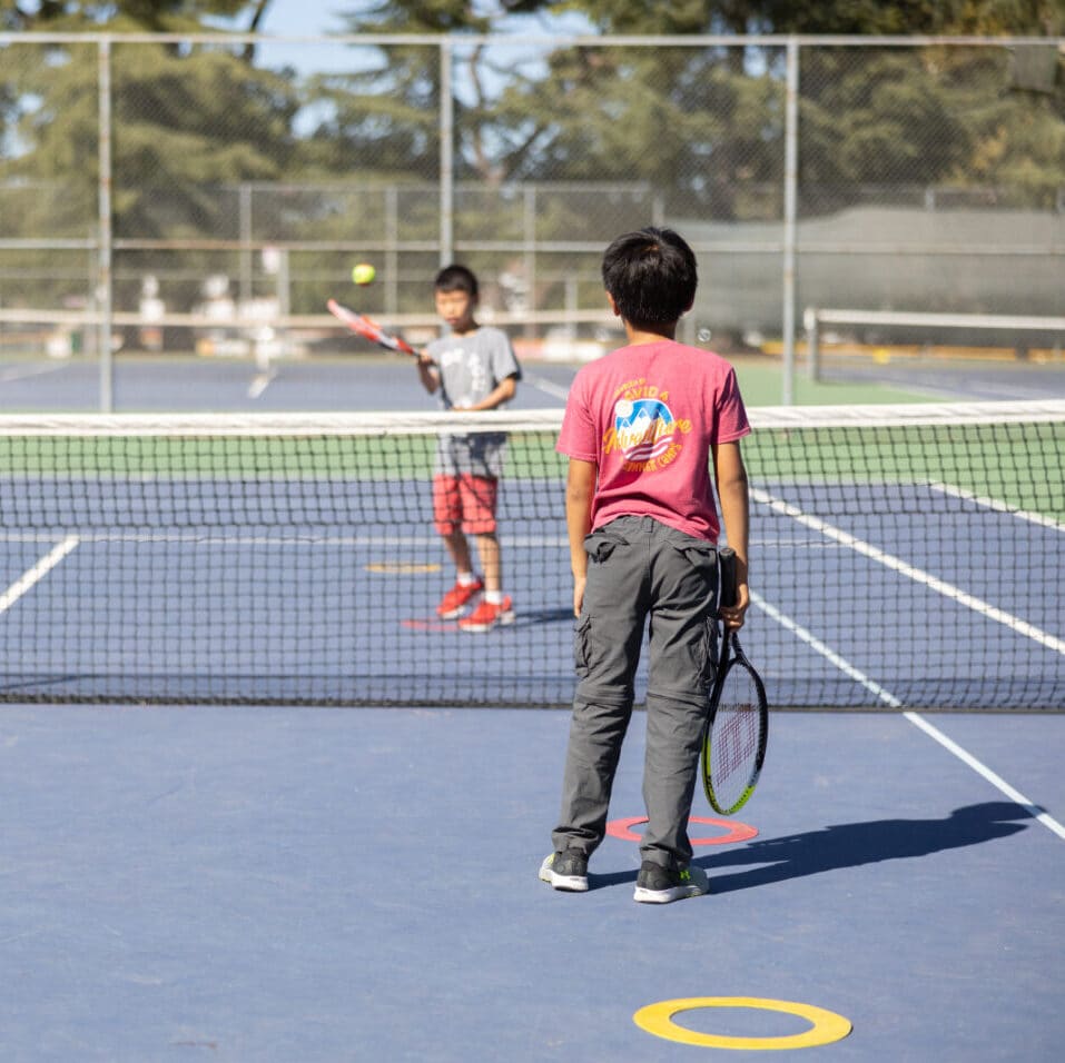 Two kids playing tennis on a hard court