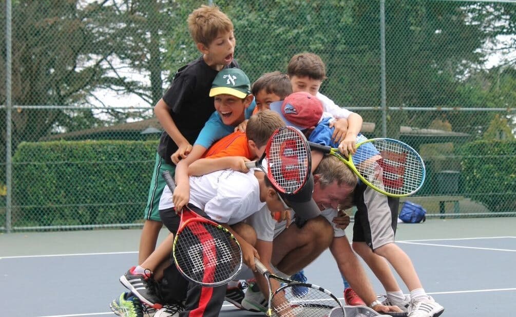 Young players laughing in a pile with their coach on the court